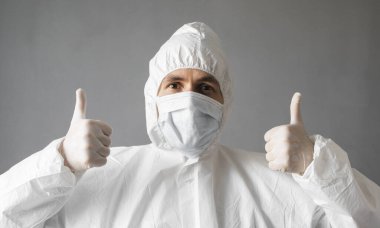 Beyaz koruyucu giysili, tıbbi maskeli ve lastik eldivenli doktor baş parmağını kaldırıyor. Koronavirüs salgını tehdidi altındayken insanlara yardım etmek. Salgın, Coronavirus covid 19 salgını..
