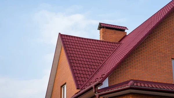Czerwony metalowy dach dachówki. Blachy dachowe. Nowoczesne rodzaje materiałów dachowych. Dach domu, dach metalowy dachówka na tle błękitnego nieba. Budowa. — Zdjęcie stockowe