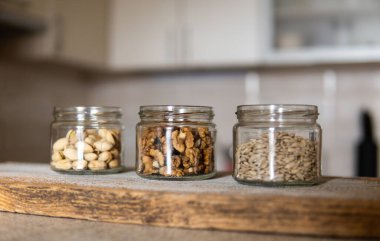 Kavanozda ayçekirdeği, ceviz ve şam fıstığı var. Arka planda mutfak olan beyaz bir şarap masasında duruyor. Fındık sağlıklı bir vejetaryen protein ve besleyici yemektir. Taşralı eski odunlarda fındıklar.