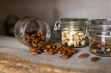 Bademler bir kavanozun içindeki beyaz şarap masasına ve diğer fındıklara saçılmış. Badem sağlıklı bir vejetaryen protein yiyeceğidir. Kırsal kesimlerdeki bademler.