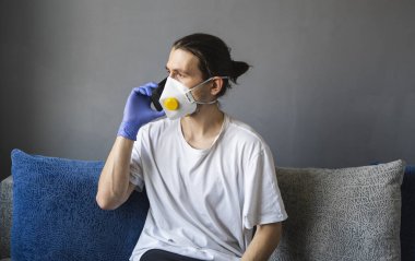 Tıbbi maskeli ve lastik eldivenli bir adam evde oturup karantina sırasında bir kanepede arkadaşlarıyla ya da iş arkadaşlarıyla konuşur. Salgın bir covid 'de uzaktan çalışan bir adam..