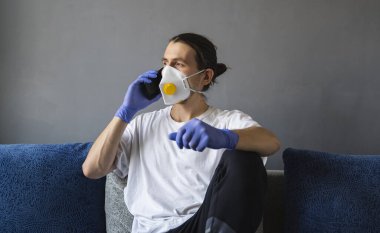 Tıbbi maskeli ve lastik eldivenli bir adam evde oturup karantina sırasında bir kanepede arkadaşlarıyla ya da iş arkadaşlarıyla konuşur. Salgın bir covid 'de uzaktan çalışan bir adam..