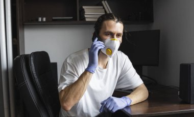 Tıbbi maskeli ve lastik eldivenli bir adam evde oturuyor ve karantina sırasında arkadaşlarıyla ya da iş ortağıyla telefonda konuşuyor. Uzaktan kumandalı bir adam salgın hastalığın pençesinde. Coronavirüs.