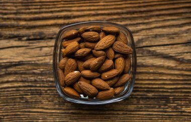 Bademler arka plan olarak eski ahşap bir masada küçük bir tabakta. Badem sağlıklı bir vejetaryen protein yiyeceğidir. Doğal çerezler.