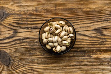 Eski ahşap bir masada, arka planda fotokopi alanı olan küçük bir tabakta şam fıstığı. Pistachio sağlıklı bir vejetaryen protein yiyeceğidir. Doğal çerezler.