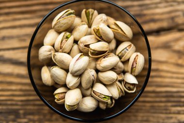 Eski ahşap bir masada, arka planda fotokopi alanı olan küçük bir tabakta şam fıstığı. Pistachio sağlıklı bir vejetaryen protein yiyeceğidir. Doğal çerezler.