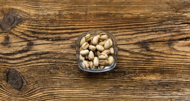 Eski ahşap bir masada, arka planda fotokopi alanı olan küçük bir tabakta şam fıstığı. Pistachio sağlıklı bir vejetaryen protein yiyeceğidir. Doğal çerezler.