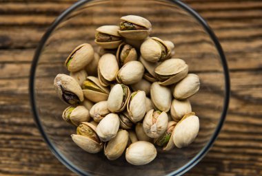 Eski ahşap bir masada, arka planda fotokopi alanı olan küçük bir tabakta şam fıstığı. Pistachio sağlıklı bir vejetaryen protein yiyeceğidir. Doğal çerezler.