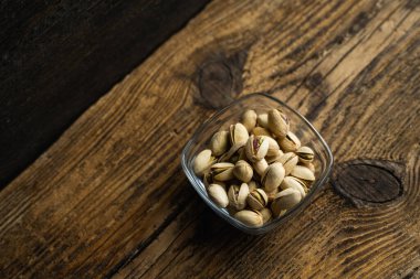Eski ahşap bir masada, arka planda fotokopi alanı olan küçük bir tabakta şam fıstığı. Pistachio sağlıklı bir vejetaryen protein yiyeceğidir. Doğal çerezler.
