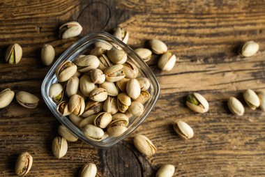 Arka plan olarak eski ahşap bir masada, bir tabağın etrafına saçılmış badem cevizleri olan küçük bir tabakta şam fıstığı. Pistachio sağlıklı bir vejetaryen protein yiyeceğidir. Doğal çerezler.