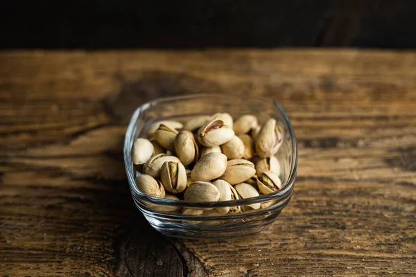 Pistachios in a small plate on a vintage wooden table as a background with a copy space. Pistachio is a healthy vegetarian protein nutritious food. Natural nuts snacks. — Stock Photo, Image