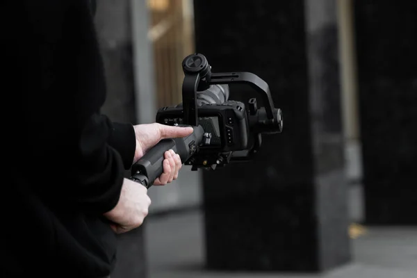 Professionele videograaf in zwarte hoodie met professionele camera op 3-assige gimbal stabilisator. Filmmaker maakt een geweldige video met een professionele filmcamera. Cinematograaf. — Stockfoto