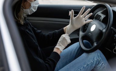 Koruyucu tıbbi maskeli kadın araba sürmeyi planlarken kendini bakteri virüsünden korumak için lastik eldiven takıyor. Karantina, salgın, covid 19, koronavirüs ve enfeksiyon sırasında koruyucu maske..