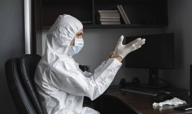 Koruyucu giysili ve tıbbi maskeli adam karantina sırasında iş yerinde lastik eldiven takıyor. Tasarımcı, sanatçı, mimar, iş adamı salgın bir covid 'de uzaktan çalışıyor..