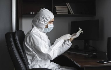 Koruyucu giysili ve tıbbi maskeli adam karantina sırasında iş yerinde lastik eldiven takıyor. Tasarımcı, sanatçı, mimar, iş adamı salgın bir covid 'de uzaktan çalışıyor..