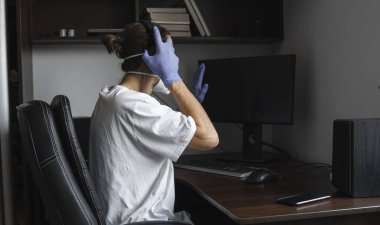 Tıbbi maskeli ve eldivenli bir adam evde oturup karantina sırasında bilgisayarda çalışıyor ve iş ortağına ya da arkadaşlarına merhaba diyor. Bir salgın covid içinde uzaktan çalışma.