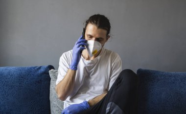 Tıbbi maskeli ve lastik eldivenli bir adam evde oturup karantina sırasında bir kanepede arkadaşlarıyla ya da iş arkadaşlarıyla konuşur. Salgın bir covid 'de uzaktan çalışan bir adam..