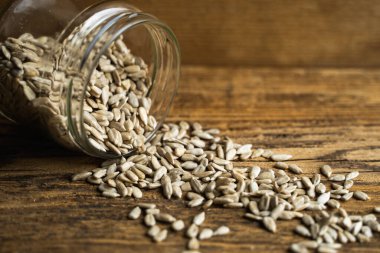 Ayçiçeği tohumları bir kavanozun içindeki ahşap şarap masasına saçılmış. Sağlıklı vejetaryen protein besleyici gıdalar. Kırsal kesimde ayçiçeği tohumu.