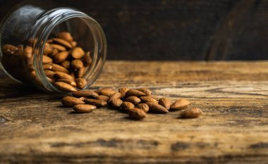 Bademler bir kavanozun içindeki ahşap şarap masasına saçılmış. Badem sağlıklı bir vejetaryen protein yiyeceğidir. Kırsal kesimlerdeki bademler.