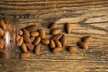 Bademler bir kavanozun içindeki ahşap şarap masasına saçılmış. Badem sağlıklı bir vejetaryen protein yiyeceğidir. Kırsal kesimlerdeki bademler.