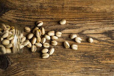 Fıstıklar bir kavanozun içindeki ahşap şarap masasına saçılmış. Pistachio sağlıklı bir vejetaryen protein yiyeceğidir. Köhne odunlarda fıstıklar.