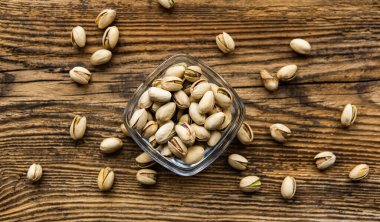 Arka plan olarak eski ahşap bir masada, bir tabağın etrafına saçılmış badem cevizleri olan küçük bir tabakta şam fıstığı. Pistachio sağlıklı bir vejetaryen protein yiyeceğidir. Doğal çerezler.