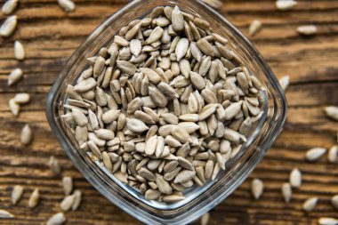 Küçük bir tabakta ayçiçeği tohumları ve ahşap şarap masasına serpiştirilmiş tohumlar. Sağlıklı vejetaryen protein besleyici gıdalar. Kırsal kesimde ayçiçeği tohumu.