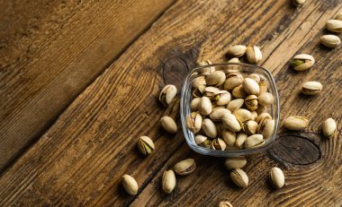 Arka plan olarak eski ahşap bir masada, bir tabağın etrafına saçılmış badem cevizleri olan küçük bir tabakta şam fıstığı. Pistachio sağlıklı bir vejetaryen protein yiyeceğidir. Doğal çerezler.