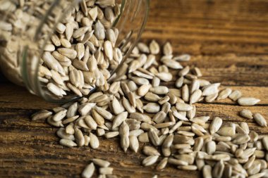 Ayçiçeği tohumları bir kavanozun içindeki ahşap şarap masasına saçılmış. Sağlıklı vejetaryen protein besleyici gıdalar. Kırsal kesimde ayçiçeği tohumu.
