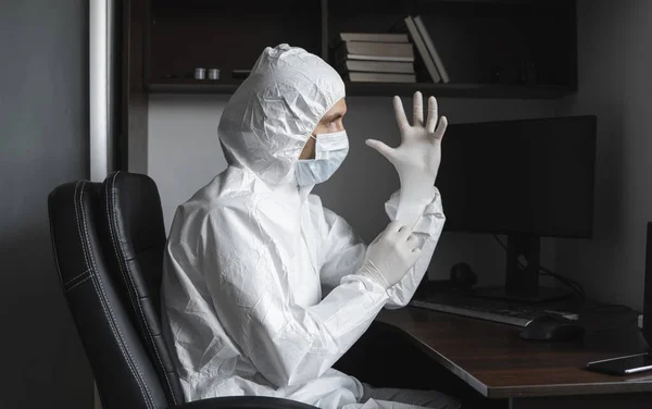 Man in protective suit and medical mask is wears rubber gloves at his working place at home during quarantine. Designer, artist, architect, businessman at remote work in a pandemic covid. — Stock Photo, Image