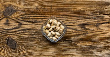 Eski ahşap bir masada, arka planda fotokopi alanı olan küçük bir tabakta şam fıstığı. Pistachio sağlıklı bir vejetaryen protein yiyeceğidir. Doğal çerezler.