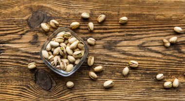 Arka plan olarak eski ahşap bir masada, bir tabağın etrafına saçılmış badem cevizleri olan küçük bir tabakta şam fıstığı. Pistachio sağlıklı bir vejetaryen protein yiyeceğidir. Doğal çerezler.
