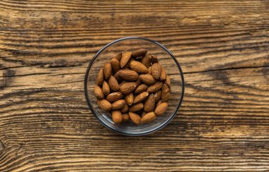 Bademler eski ahşap bir masada küçük bir tabakta fotokopi alanı ile arka plan olarak kullanılıyor. Badem sağlıklı bir vejetaryen protein yiyeceğidir. Doğal çerezler.