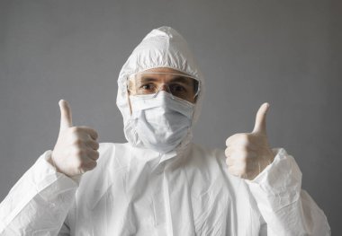 Beyaz koruyucu giysili, tıbbi maskeli ve lastik eldivenli doktor baş parmağını kaldırıyor. Koronavirüs salgını tehdidi altındayken insanlara yardım etmek. Salgın, Coronavirus covid 19 salgını..