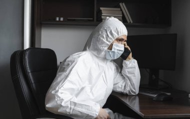 Tıbbi maskeli ve lastik eldivenli bir adam evde oturuyor ve karantina sırasında arkadaşlarıyla ya da iş ortağıyla telefonda konuşuyor. Uzaktan kumandalı bir adam salgın hastalığın pençesinde. Coronavirüs.