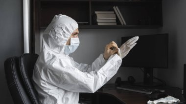 Koruyucu giysili ve tıbbi maskeli adam karantina sırasında iş yerinde lastik eldiven takıyor. Tasarımcı, sanatçı, mimar, iş adamı salgın bir covid 'de uzaktan çalışıyor..