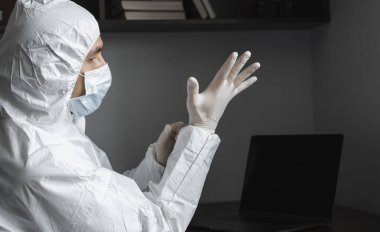 Koruyucu giysili ve tıbbi maskeli adam karantina sırasında iş yerinde lastik eldiven takıyor. Tasarımcı, sanatçı, mimar, iş adamı salgın bir covid 'de uzaktan çalışıyor..