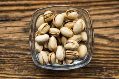 Eski ahşap bir masada, arka planda fotokopi alanı olan küçük bir tabakta şam fıstığı. Pistachio sağlıklı bir vejetaryen protein yiyeceğidir. Doğal çerezler.