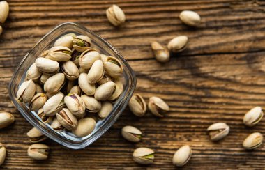 Arka plan olarak eski ahşap bir masada, bir tabağın etrafına saçılmış badem cevizleri olan küçük bir tabakta şam fıstığı. Pistachio sağlıklı bir vejetaryen protein yiyeceğidir. Doğal çerezler.