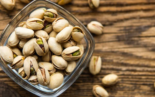 Pistazien in einem kleinen Teller mit verstreuten Mandelnüssen um einen Teller herum auf einem alten Holztisch als Hintergrund. Pistazie ist eine gesunde vegetarische Proteinnahrung. Natürliche Nüsse Snacks. — Stockfoto