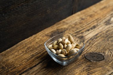 Eski ahşap bir masada, arka planda fotokopi alanı olan küçük bir tabakta şam fıstığı. Pistachio sağlıklı bir vejetaryen protein yiyeceğidir. Doğal çerezler.