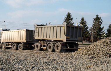 Bir çöp kamyonu inşaat alanına çakıl döküyor. Çöp kamyonu çakıl yükünü yeni bir yol yapım projesine boşaltıyor. Yol yapımı. Asfalt için temel hazırlama.