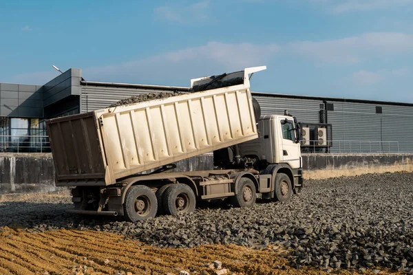 Een vuilniswagen dumpt grind op een bouwplaats. Dump truck dumpt zijn lading grind op een nieuw wegenbouwproject. Wegenbouw. Voorbereiding van het fundament voor een asfalt. — Stockfoto