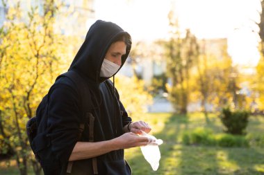 Siyah kapüşonlu, tıbbi maskeli bir adam mikropları, zehirli dumanları ve tozu önlemek için lastik eldiven giyiyor. Bakteriyel Coronavirus ya da Covid 19 salgınının önlenmesi. Küresel Karantina.