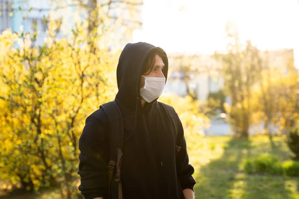 Hombre con capucha negra usando una máscara médica para prevenir gérmenes, humos tóxicos, polvo. Prevención de la infección bacteriana Virus Corona o epidemia de Covid 19 en una calle. Cuarentena mundial pandémica por Coronavirus . — Foto de Stock