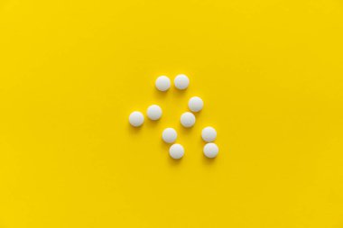 Sarı arka planda beyaz haplar. İlaç, ilaç, ağrı kesici, tablet, ilaçlar, antibiyotik, vitamin, tedavi. Eczane temalı. Beyaz yüzeye saçılmış hapların üst görüntüsü.
