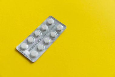 Paketteki hapların üst görüntüsü. Sarı arka planda beyaz haplar. İlaç, ilaç, ağrı kesici, tablet, ilaçlar, ilaçlar, antibiyotik, vitamin, tedavi, kapsül, doz. Eczane teması.