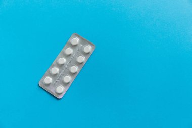 Paketteki hapların üst görüntüsü. Mavi arka planda beyaz haplar. İlaç, ilaç, ağrı kesici, tablet, ilaçlar, ilaçlar, antibiyotik, vitamin, tedavi, kapsül, doz. Eczane teması.