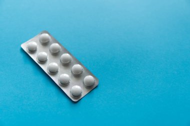 Paketteki hapların üst görüntüsü. Mavi arka planda beyaz haplar. İlaç, ilaç, ağrı kesici, tablet, ilaçlar, ilaçlar, antibiyotik, vitamin, tedavi, kapsül, doz. Eczane teması.