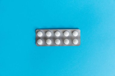 Paketteki hapların üst görüntüsü. Mavi arka planda beyaz haplar. İlaç, ilaç, ağrı kesici, tablet, ilaçlar, ilaçlar, antibiyotik, vitamin, tedavi, kapsül, doz. Eczane teması.